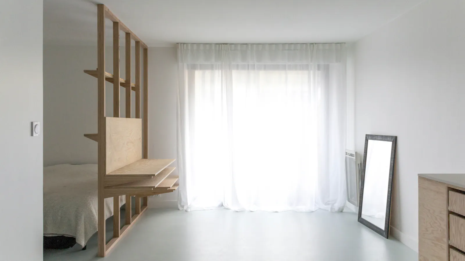 Cugnaux — Pièce de vie avec grand voilage clair et meuble en bois séparant le coin nuit