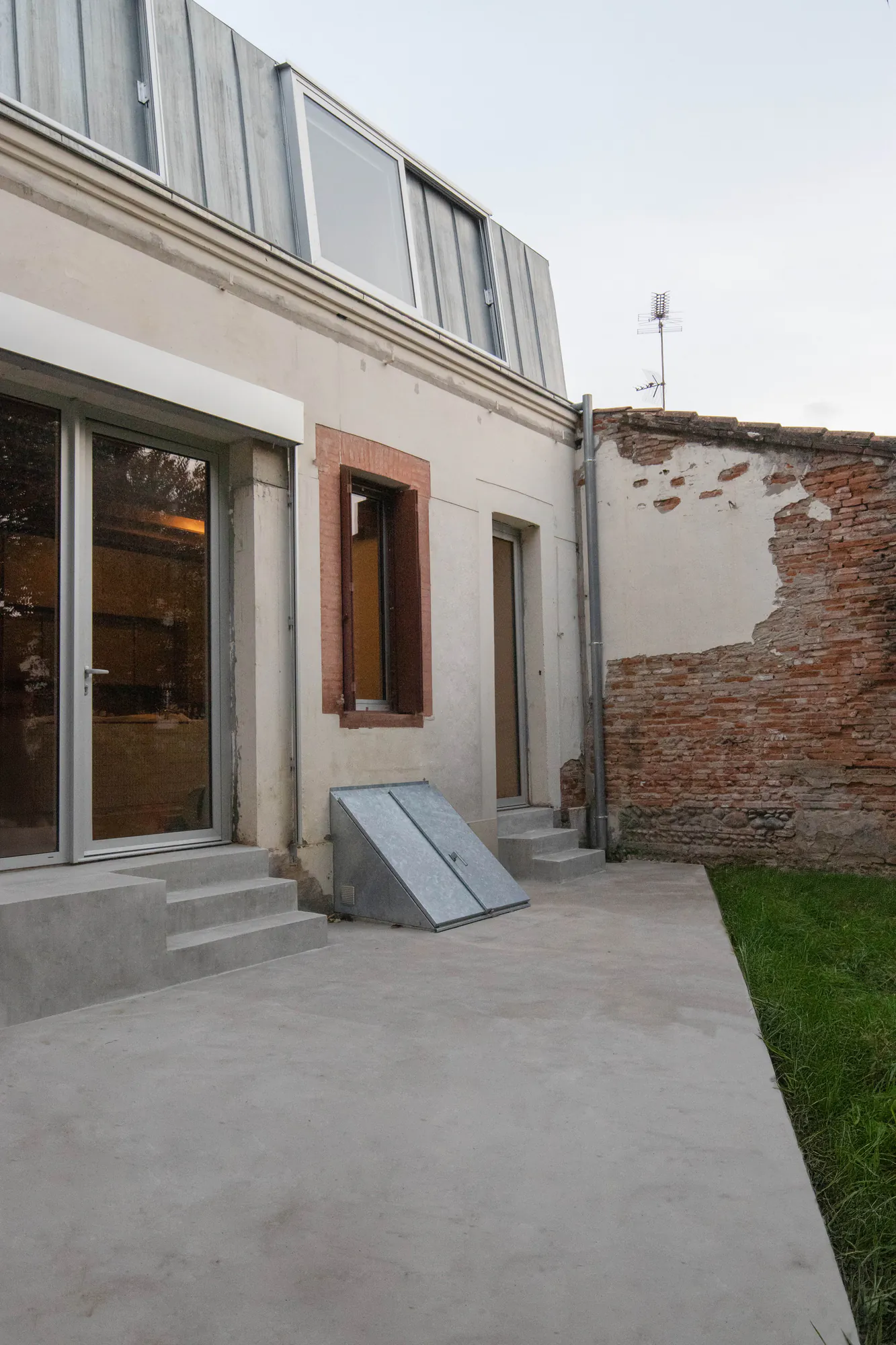 Negreneys — Façade sur jardin, baie vitrée et terrasse en béton sous la surélévation en zinc