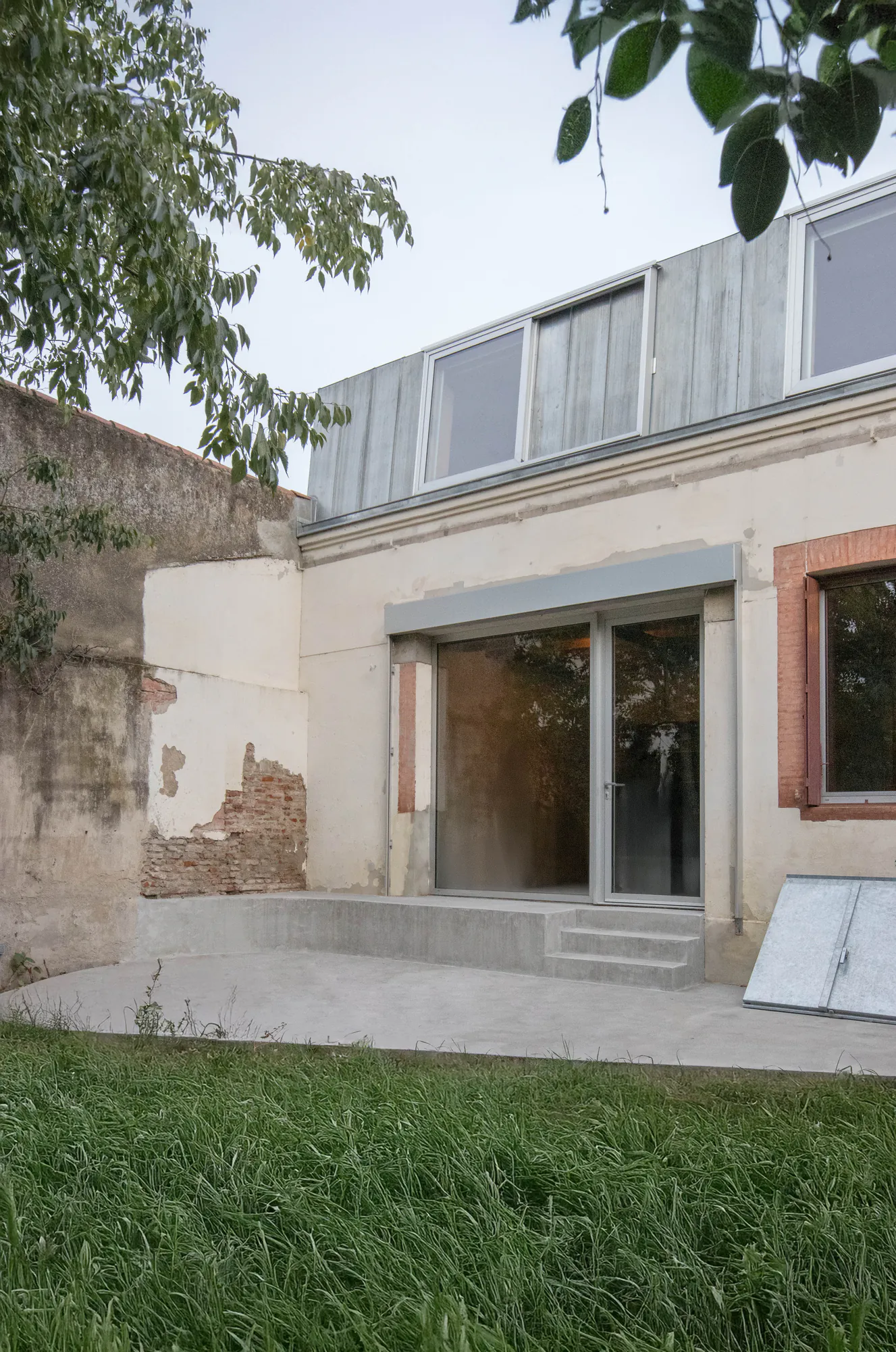 Negreneys — Façade sur jardin vue en biais, terrasse en béton et mur ancien en brique
