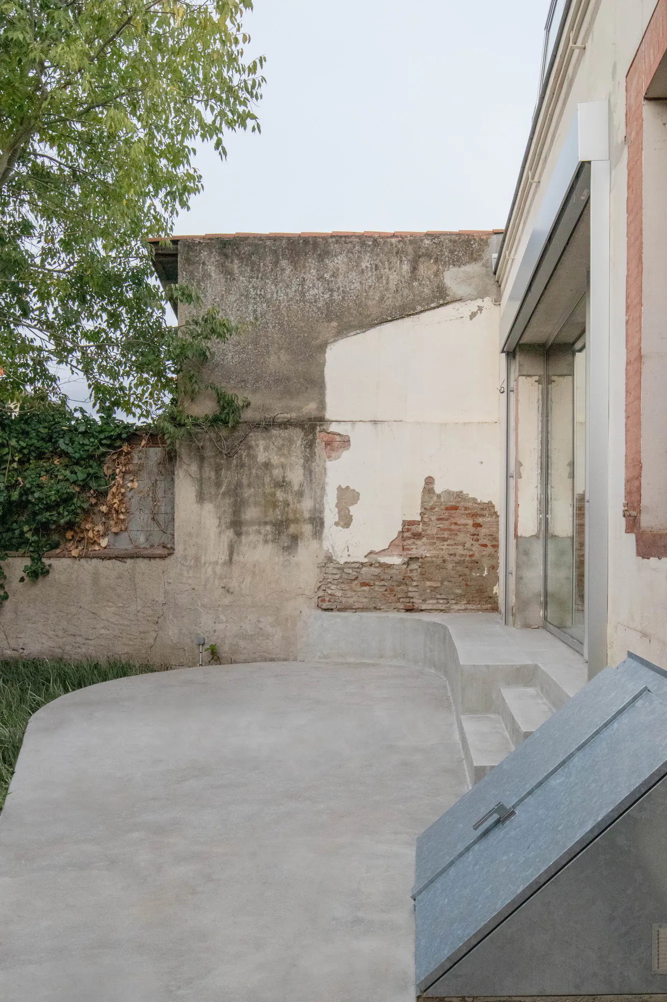 Negreneys — Terrasse en béton arrondie le long de la façade, devant le mur de clôture ancien