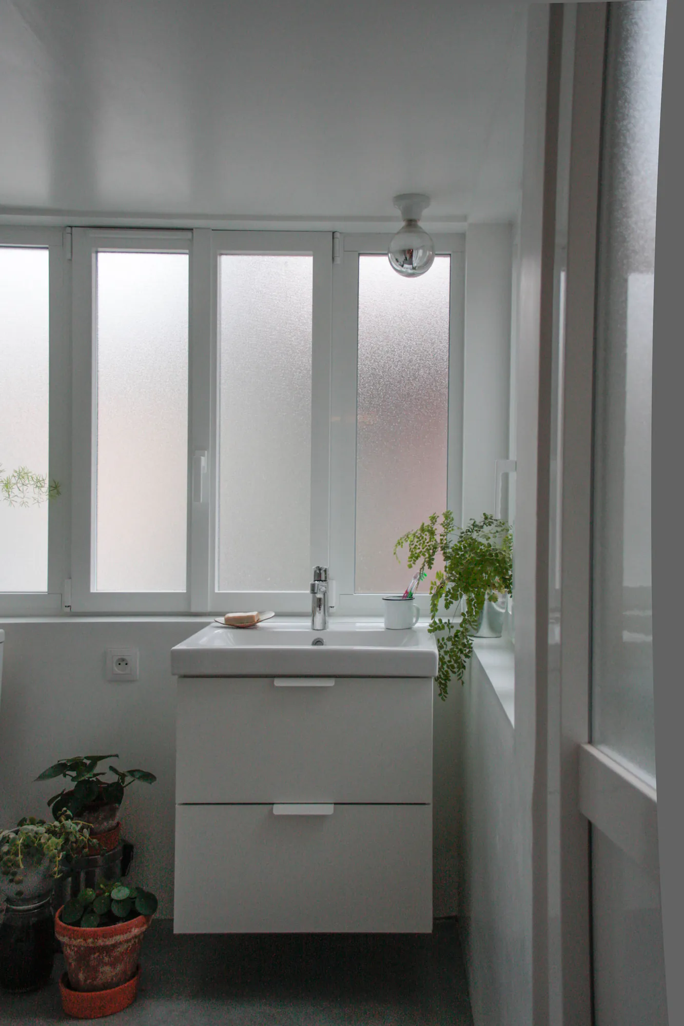 République — Salle de bains, meuble vasque blanc, plantes et fenêtre en verre dépoli